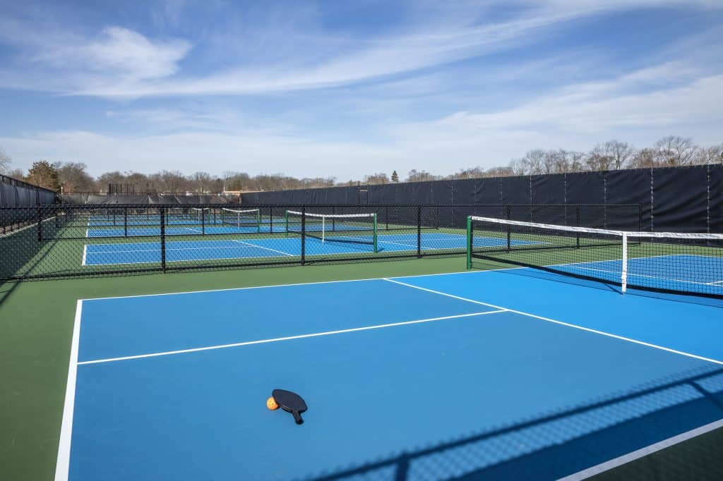 Outdoor pickleball courts with blue and green surfaces, fenced for play.