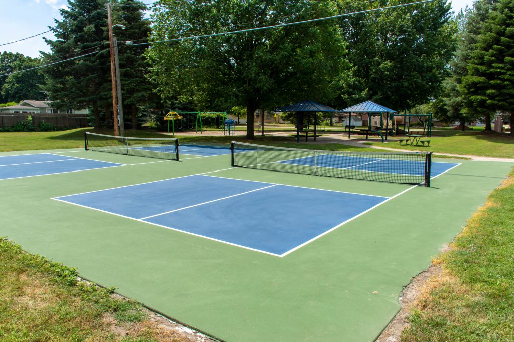 A vibrant, well-maintained pickleball court, with a bright blue surface, white boundary lines, and a sturdy net stretched across the center.