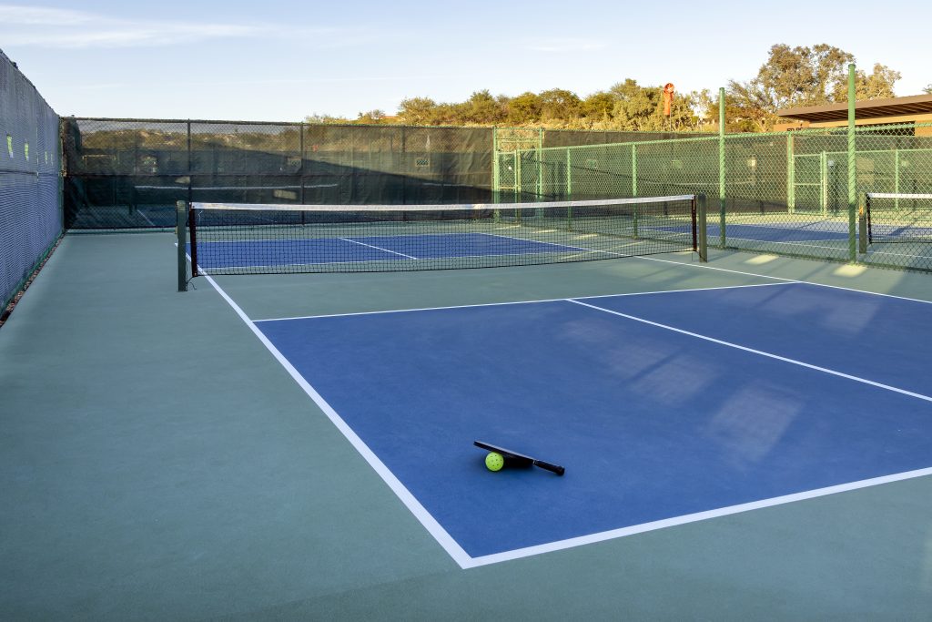 A vibrant pickleball court with a bright yellow ball at the center.