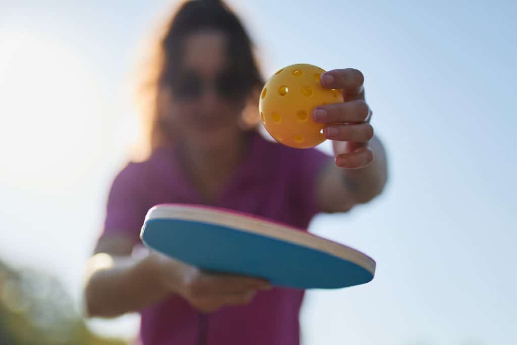 A person holding a pickleball and paddle, ready to serve, emphasizing the preparation for a pickleball game.